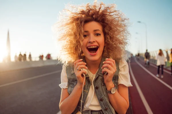 Счастливая молодая девушка на улице. Красивая блондинка с наушниками и смартфоном . — стоковое фото