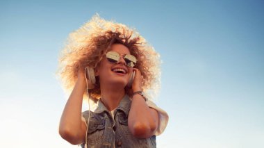 Sevimli Kıvırcık sarışın müzik dinleyin. Genç kadın büyük kulaklıklar ile. trendy kız açık havada portresi