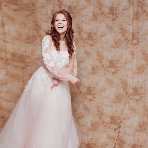 Gelukkig lachen jonge vrouw in de bruiloft jurk met lange mouwen. Jonge roodharige vrouw in trouwjurk — Stockfoto