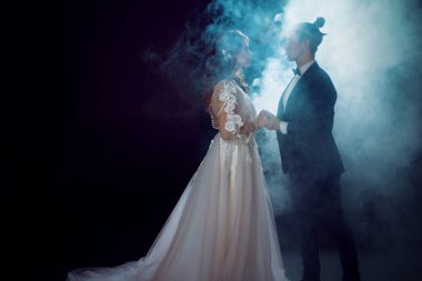 Gelin ve damat birbirlerine bakıyorlar. Duman koyu arka plan üzerinde romantik gizemli portre. Erkek ve kadın, gelinlik.