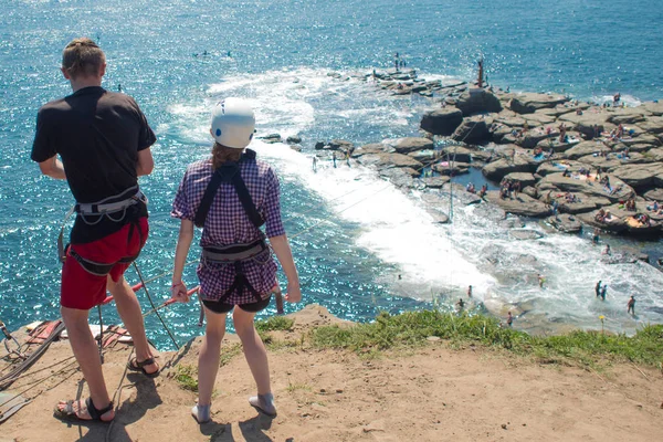 Two are preparing to jump with a bungee from a cliff above the sea, back view, — Stock Photo, Image