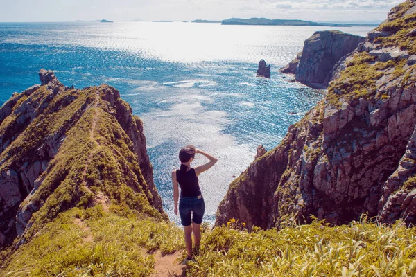 Lonely girl standing on a rocky shore and looking into the distance. Girl on background of beautiful wildlife, sea and rocks — Stock Photo, Image