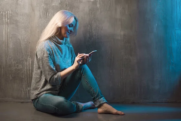 Una mujer joven utiliza un teléfono inteligente, tonificación azul — Foto de Stock