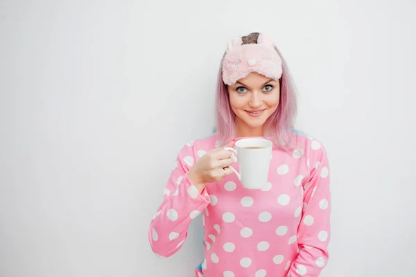 Boldog fiatal nő reggel kávét iszik. Gyönyörű lány rózsaszín pizsama és sleepmask — Stock Fotó
