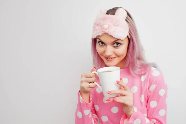 Ελκυστικό κορίτσι στο ροζ πιτζάμες και μάσκα ύπνου, απολαμβάνοντας τον πρωινό καφέ — Φωτογραφία Αρχείου