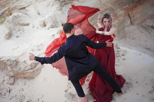 Amor e paixão, conceito. Belo jovem casal dançando no deserto. O homem de preto e a mulher de vermelho — Fotografia de Stock