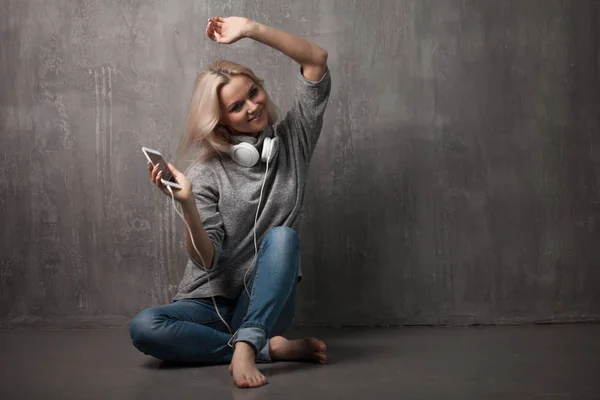 Mujer joven y atractiva con smartphone y auriculares grandes, sentada en el suelo. Música en la aplicación móvil . —  Fotos de Stock