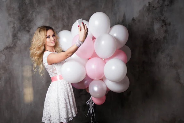 Charmante jonge blonde in een witte jurk met roze ballonnen, maken een selfie — Stockfoto