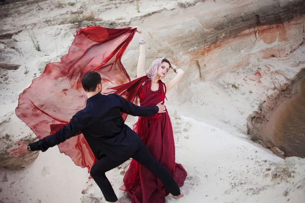 Amor e paixão, conceito. Belo jovem casal dançando no deserto. O homem de preto e a mulher de vermelho — Fotografia de Stock