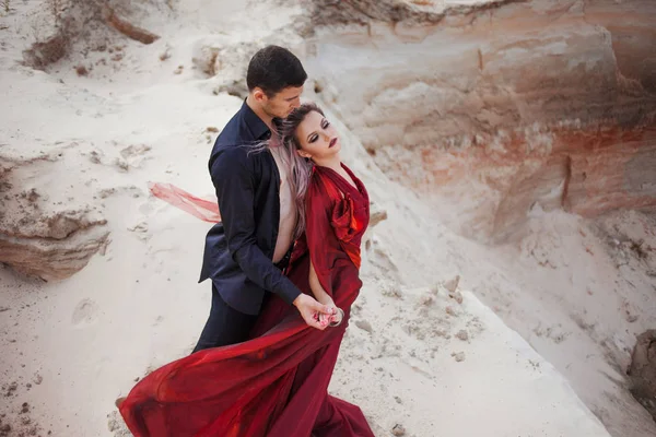 Liefde en passie, concept. Mooie jong koppel dansen in de woestijn. De man in het zwart en vrouw in het rood — Stockfoto