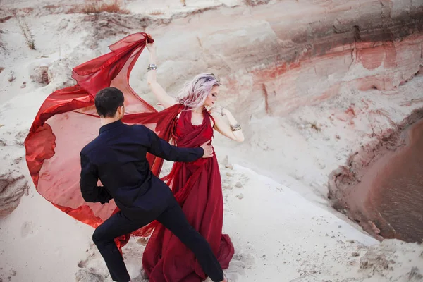 Amor e paixão, conceito. Belo jovem casal dançando no deserto. O homem de preto e a mulher de vermelho — Fotografia de Stock