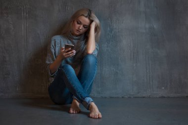 Helpline, psychological assistance. Suffering young woman sitting in a corner with a phone in her hand clipart