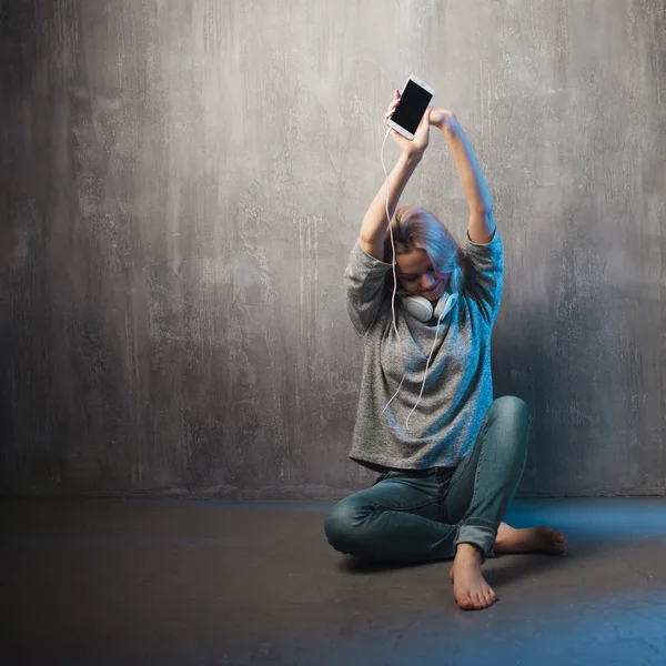 Mulher jovem e atraente com smartphone e fones de ouvido grandes, sentado no chão. Música no aplicativo móvel . — Fotografia de Stock