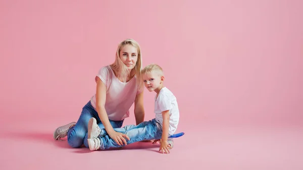 Молодая позитивная мать с маленьким сыном. Красивая блондинка со своим ребенком на скейтборде — стоковое фото