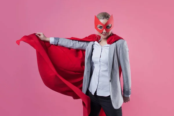 Joven mujer atractiva superhéroe. Chica en un traje de negocios y una máscara con capa roja de héroe . — Foto de Stock