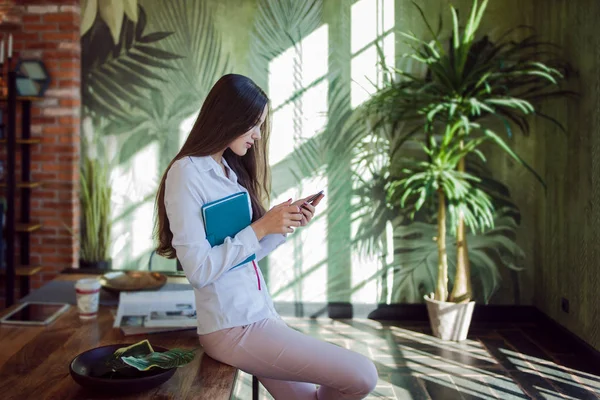 Business brunette works on the Internet, Uses smartphone sitting on the table