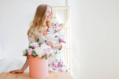 Bir şapka kutusunda çiçekli mutlu sarışın kadın modern bir ofiste. Peonies buket.