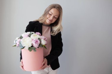 Sevimli sarışın kadın bir şapka kutusunda çiçekli. Peonies buket. Kız, iş tarzında çiçekler alır veya verir