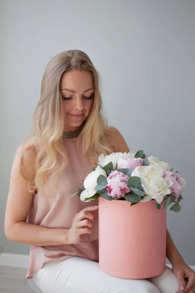 Onnellinen blondi, jolla on kukkia hattulaatikossa. Kukkakimppu pioneja. Tyttö vaaleanpunainen kimppu pioneja — kuvapankkivalokuva
