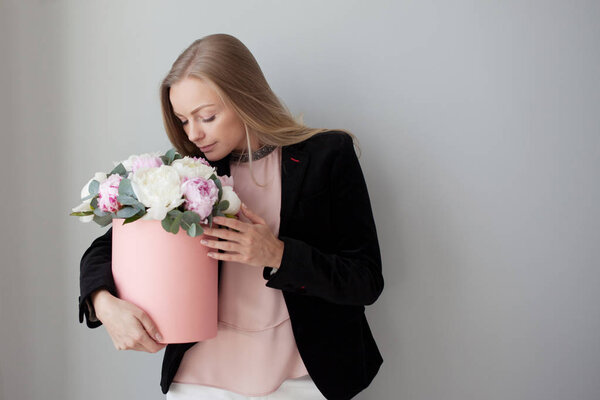 Charming blonde woman with flowers in a hat box. Bouquet of peonies. Girl in business style, receives flowers or gives