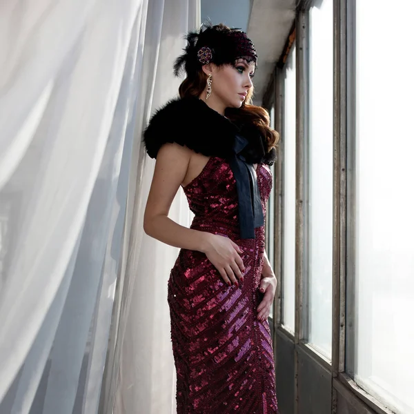 Preciosa joven en un vestido de silueta borgoña cerca de la ventana, estilo retro —  Fotos de Stock