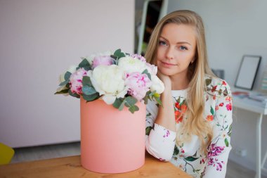 Bir şapka kutusunda çiçekli mutlu sarışın kadın modern bir ofiste. Peonies buket.