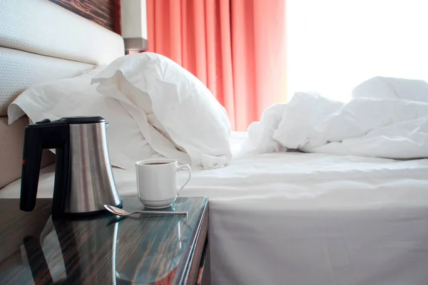 Гостиничный номер утром, кровать после сна, кровать и чашка на тумбочке — стоковое фото