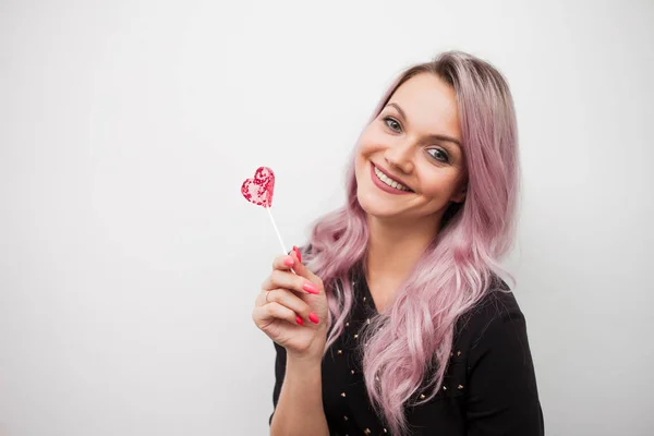 Menina encantadora encantadora com um pirulito na forma de coração. Retrato de uma jovem mulher com cabelo rosa e doce rosa — Fotografia de Stock