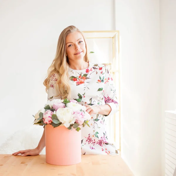 Onnellinen blondi nainen modernissa toimistossa kukkia hattulaatikossa. Kukkakimppu pioneja . — kuvapankkivalokuva