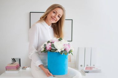 Şık Genç Sarışın ofis, beyaz gömlek ve pantolon. Mavi şapka kutusunda peonies lüks bir buket tutar.