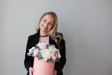 Sevimli sarışın kadın bir şapka kutusunda çiçekli. Peonies buket. Kız, iş tarzında çiçekler alır veya verir
