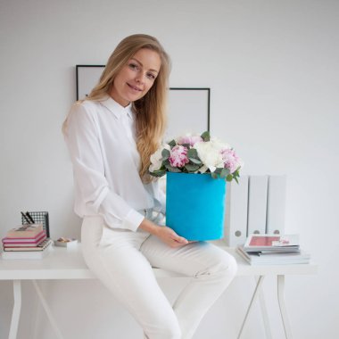 Şık Genç Sarışın ofis, beyaz gömlek ve pantolon. Mavi şapka kutusunda peonies lüks bir buket tutar.