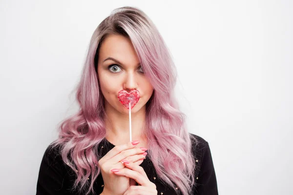 Очаровательная девушка с Lollipop в виде сердца. Портрет молодой женщины с розовыми волосами и розовыми конфетами — стоковое фото