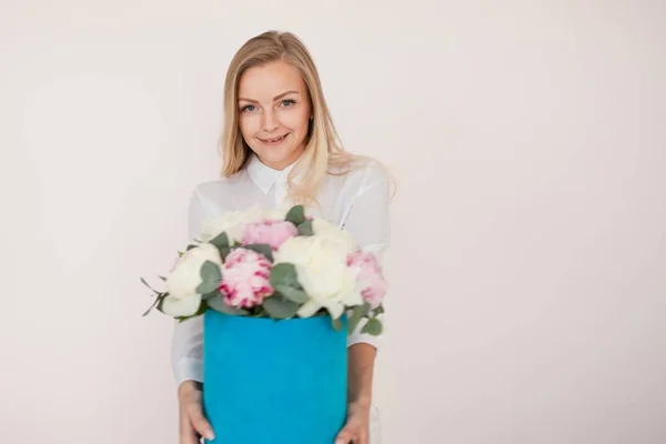 Mulher com flores numa caixa de chapéu. Buquê de peônias. Menina em estilo de negócio, recebe flores ou dá, caixa azul . — Fotografia de Stock