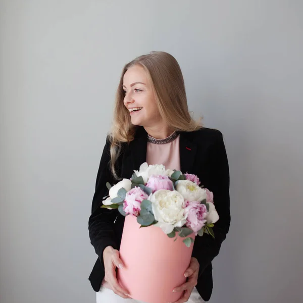 Charming blonde woman with flowers in a hat box. Bouquet of peonies. Girl in business style, receives flowers or gives — Stock Photo, Image