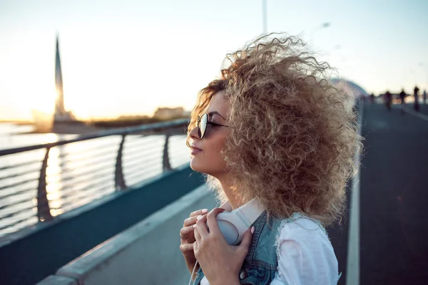 Chica de moda con auriculares grandes y gafas de sol en un paseo por la ciudad, retrato de mujer joven en perfil — Foto de Stock