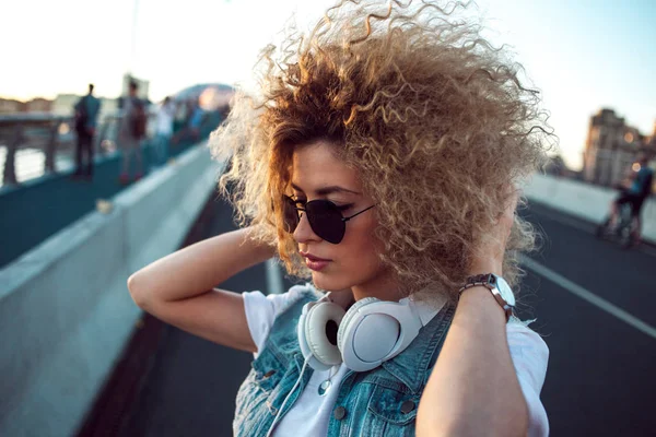 Chica de moda con auriculares grandes y gafas de sol en un paseo por la ciudad, retrato de mujer joven en perfil — Foto de Stock