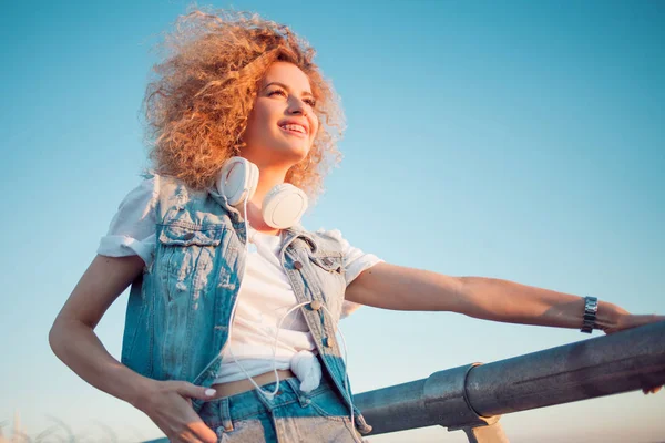 Trendy girl with large headphones on sky background, free space on the right. — Stock Photo, Image