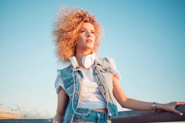 Trendy meisje met grote koptelefoon op hemelachtergrond, vrije ruimte aan de rechterkant. — Stockfoto