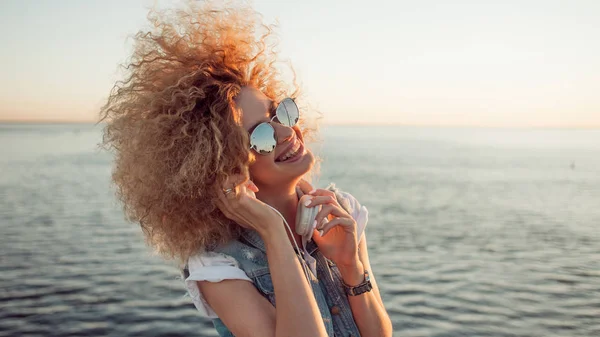 Chica de moda con auriculares grandes y gafas de sol en un paseo por la ciudad, de cerca — Foto de Stock