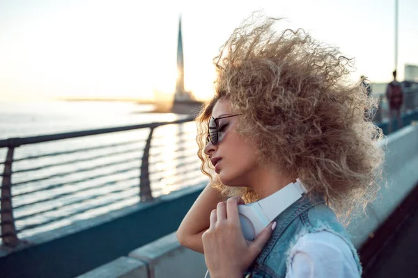 Chica de moda con auriculares grandes y gafas de sol en un paseo por la ciudad, retrato de mujer joven en perfil — Foto de Stock