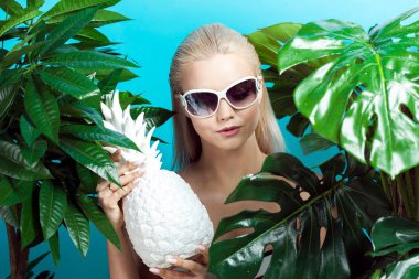 Mavi zemin üzerine mavi bikinili genç kadın. Güneş gözlüğü ve beyaz ananas ile kız