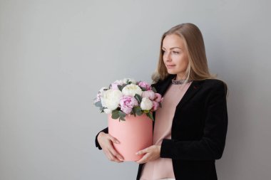 Sevimli sarışın kadın bir şapka kutusunda çiçekli. Peonies buket. Kız, iş tarzında çiçekler alır veya verir