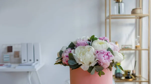 Flower delivery to the office. Working space, table with notebooks and magazines. A luxurious bouquet of peonies