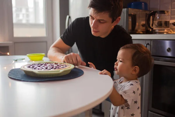 Padre e hijo en la cocina. niño quiere un delicioso pastel caliente . — Foto de Stock