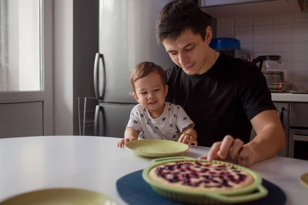 Padre e hijo en la cocina. niño quiere un delicioso pastel caliente . — Foto de Stock