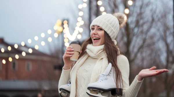 ニットのセーターと帽子で幸せな若い女スケートだし、コーヒーを飲む — ストック写真