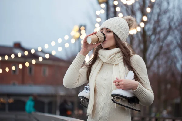 Glad ung kvinna i stickad tröja och hatt kommer skridskoåkning och dricker kaffe — Stockfoto