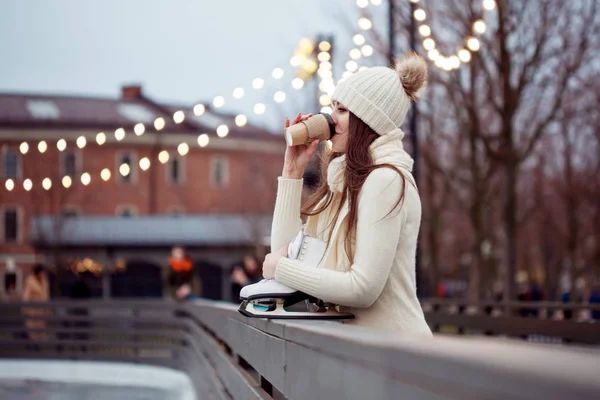 ニットのセーターと帽子で幸せな若い女スケートだし、コーヒーを飲む — ストック写真
