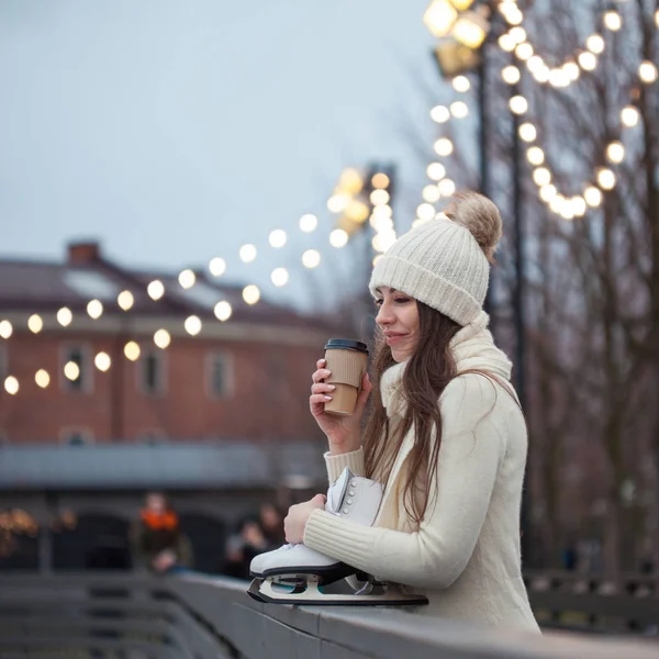 Gelukkig jonge vrouw in gebreide trui en muts gaat schaatsen en drinkt koffie — Stockfoto